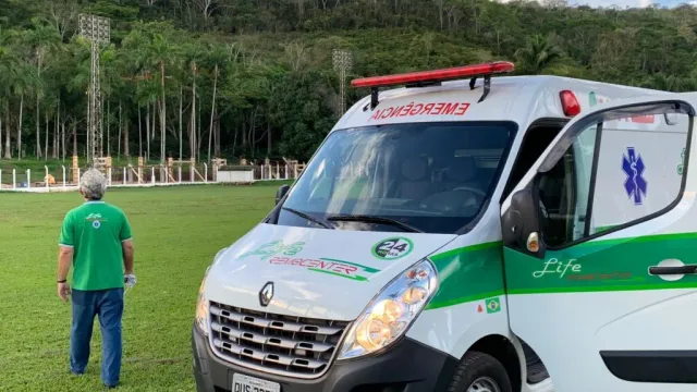 Ambulância da Life Remocenter estacionada em campo gramado, com socorrista uniformizado ao lado